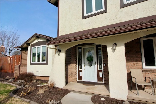 view of exterior entry with brick siding, stucco siding, and fence