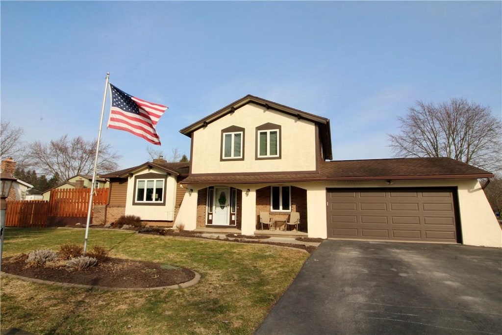 traditional home featuring stucco siding, a front lawn, driveway, fence, and a garage