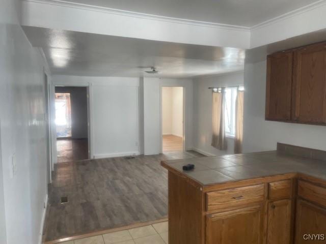 kitchen with crown molding, open floor plan, tile countertops, a peninsula, and brown cabinetry