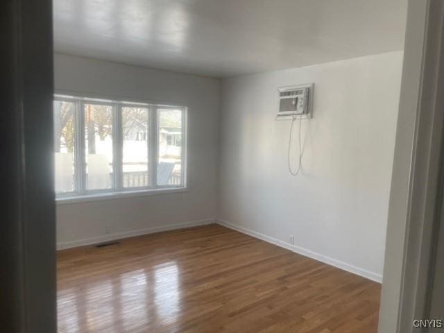 spare room featuring a wall mounted AC, baseboards, and wood finished floors