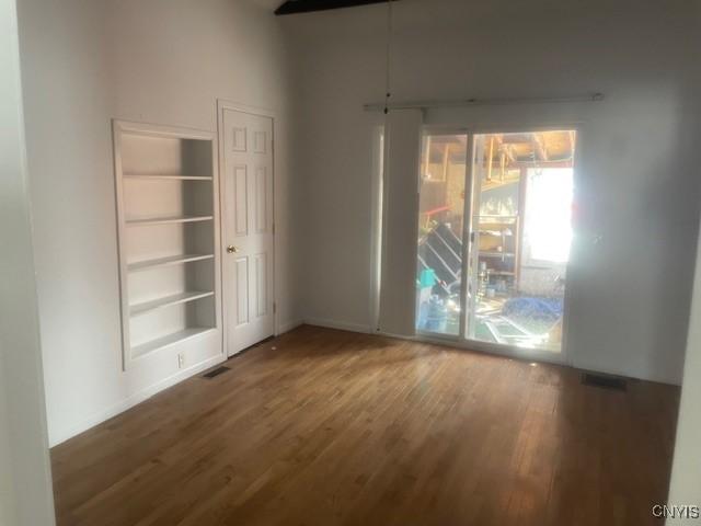spare room featuring built in shelves, wood finished floors, and visible vents