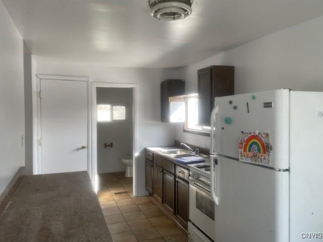 kitchen with light tile patterned floors, freestanding refrigerator, a sink, stainless steel range, and dark brown cabinetry