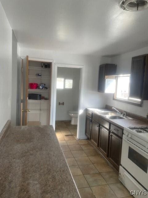 kitchen with light tile patterned flooring, white range with gas cooktop, and a sink