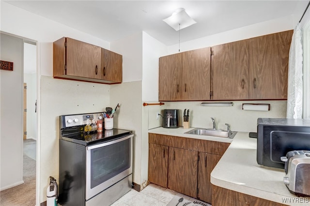 kitchen featuring light countertops, light tile patterned floors, brown cabinets, stainless steel electric range, and a sink