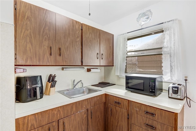 kitchen featuring brown cabinets, light countertops, black microwave, and a sink