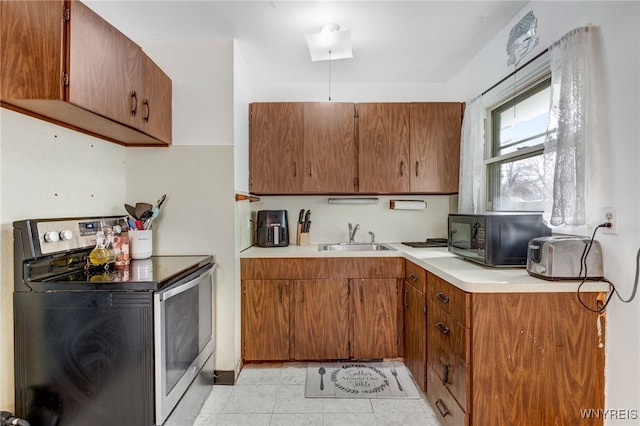 kitchen with a sink, stainless steel range with electric cooktop, brown cabinetry, light countertops, and black microwave