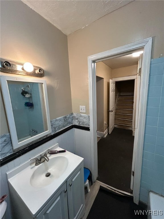 full bath featuring a wainscoted wall, a textured ceiling, vanity, and a shower