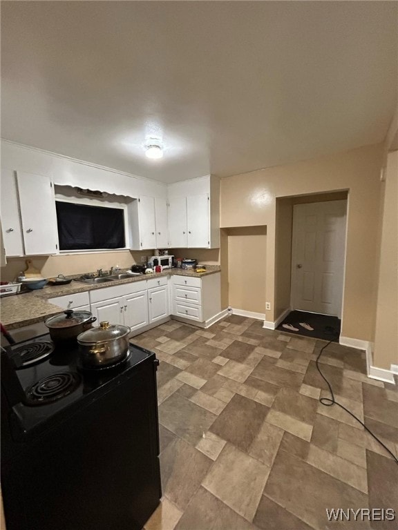 kitchen featuring a sink, baseboards, black range with electric stovetop, and white cabinetry