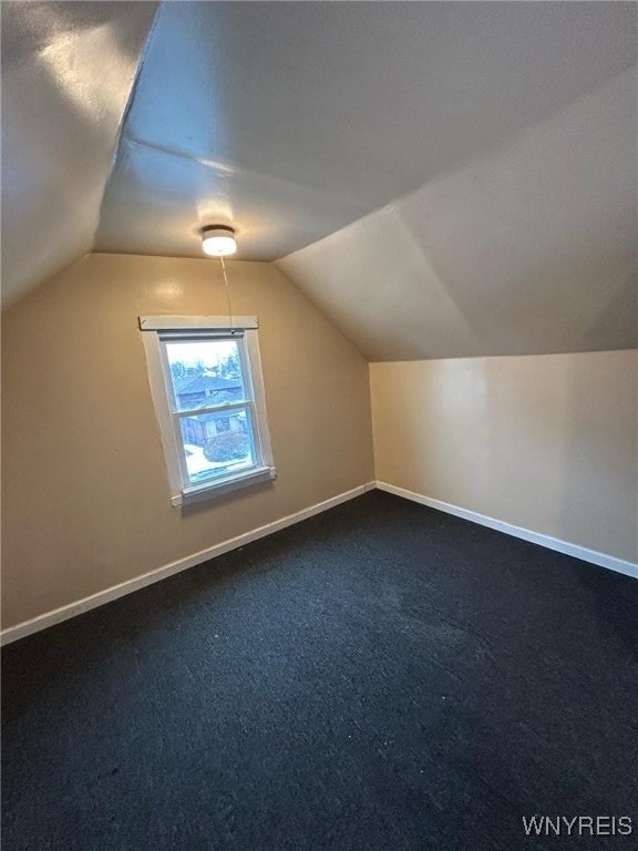 additional living space with dark carpet, lofted ceiling, and baseboards