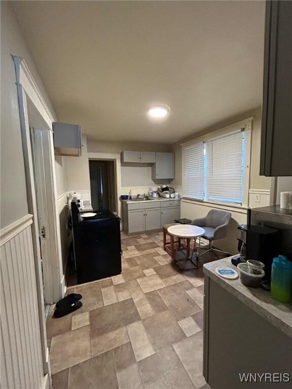 kitchen featuring wainscoting, gray cabinetry, stone finish flooring, and a sink