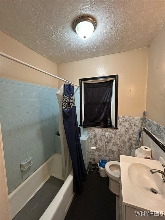 full bath with toilet, vanity, shower / bath combo, wainscoting, and a textured ceiling