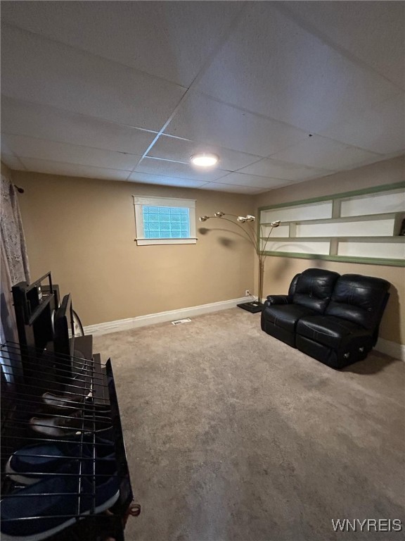basement featuring a drop ceiling, baseboards, and carpet floors