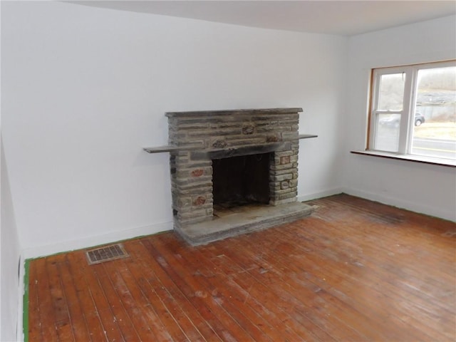 unfurnished living room with visible vents, baseboards, a stone fireplace, and hardwood / wood-style floors