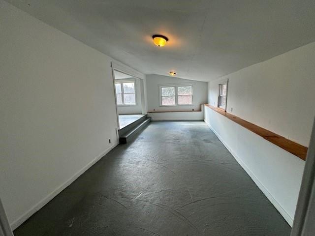 unfurnished room with lofted ceiling, baseboards, and concrete floors