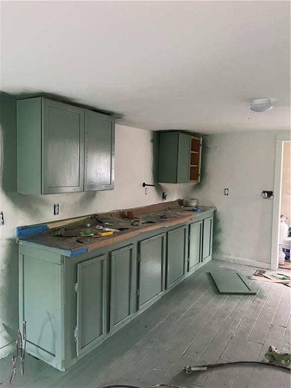 kitchen featuring dark wood finished floors, green cabinets, and baseboards