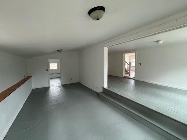 unfurnished room with stairway, finished concrete flooring, and baseboards