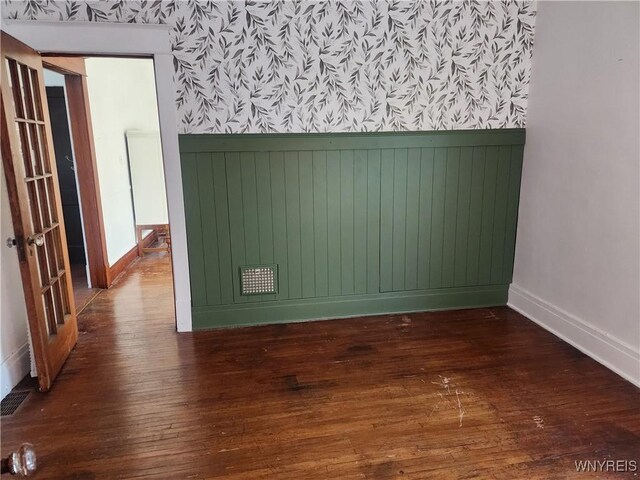 empty room with wainscoting, wallpapered walls, baseboards, and hardwood / wood-style floors