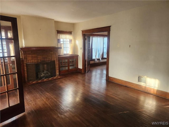 unfurnished living room with visible vents, baseboards, a brick fireplace, and wood finished floors