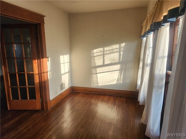 empty room with a wealth of natural light, visible vents, baseboards, and dark wood-style flooring