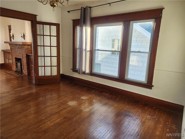 unfurnished living room with dark wood finished floors, an inviting chandelier, a brick fireplace, and baseboards