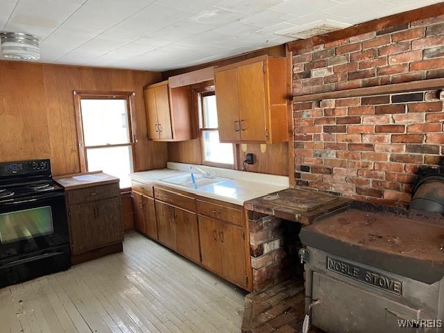 kitchen with electric range, light countertops, light wood finished floors, a sink, and brown cabinetry