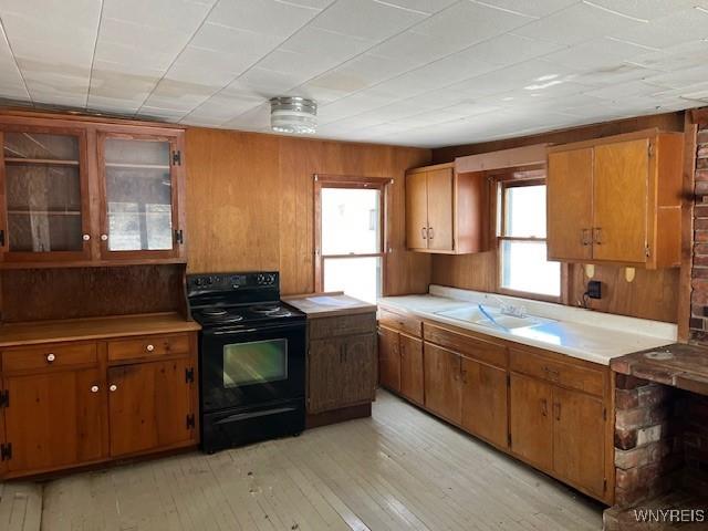 kitchen with electric range, a sink, light countertops, brown cabinets, and wooden walls
