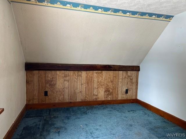 bonus room featuring dark carpet, lofted ceiling, wood walls, and baseboards