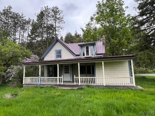 view of front of house featuring a porch, a chimney, metal roof, and view of wooded area