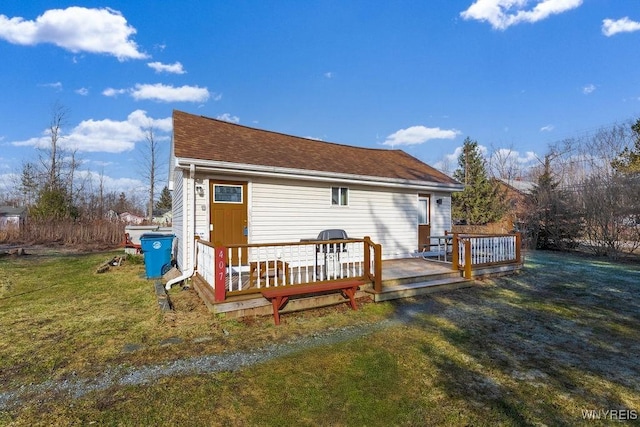 rear view of property with a lawn, a wooden deck, and roof with shingles
