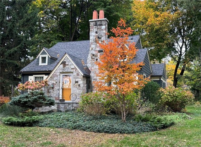 view of front of property featuring a shingled roof, stone siding, and a chimney