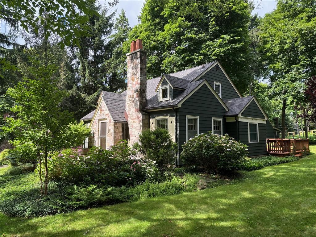 exterior space with a yard, a shingled roof, a chimney, stone siding, and a deck