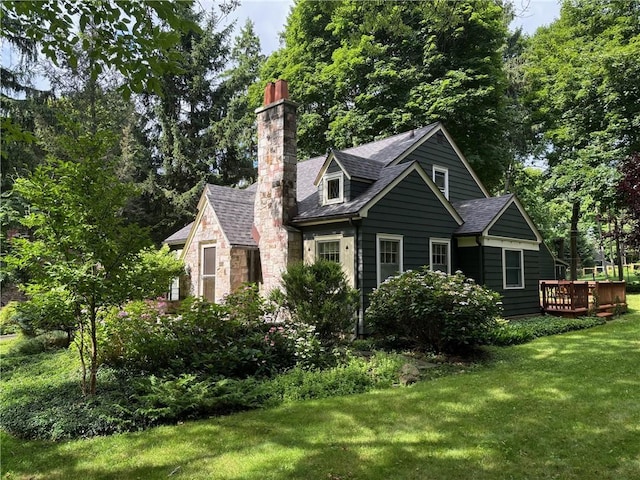 exterior space with a yard, a shingled roof, a chimney, stone siding, and a deck