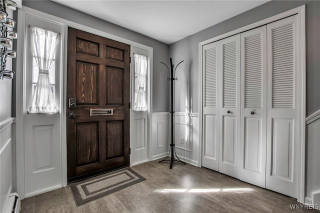 foyer with a baseboard radiator, wood finished floors, wainscoting, and a decorative wall