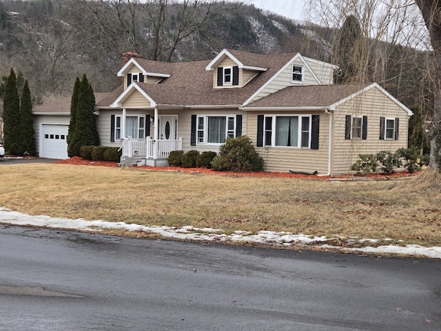 cape cod home featuring a mountain view, a shingled roof, an attached garage, and a front lawn