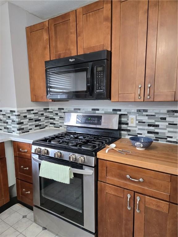 kitchen with light countertops, stainless steel gas stove, decorative backsplash, black microwave, and brown cabinets