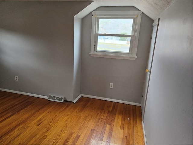 spare room with baseboards, lofted ceiling, visible vents, and hardwood / wood-style flooring
