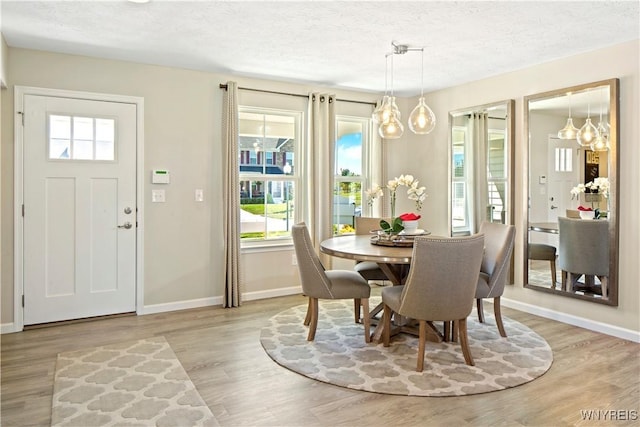dining room featuring light wood-style flooring, baseboards, and a textured ceiling