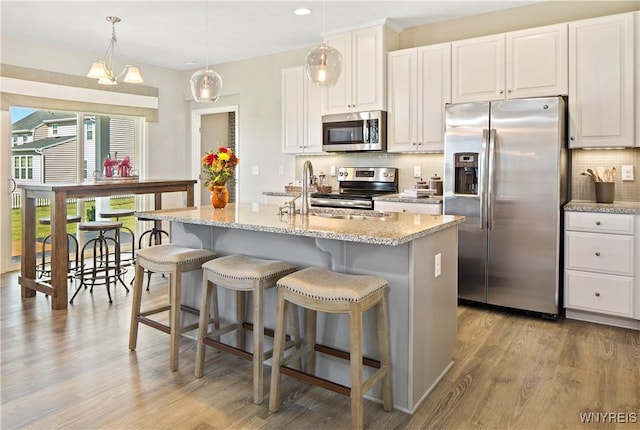 kitchen with light wood finished floors, backsplash, white cabinets, stainless steel appliances, and a sink