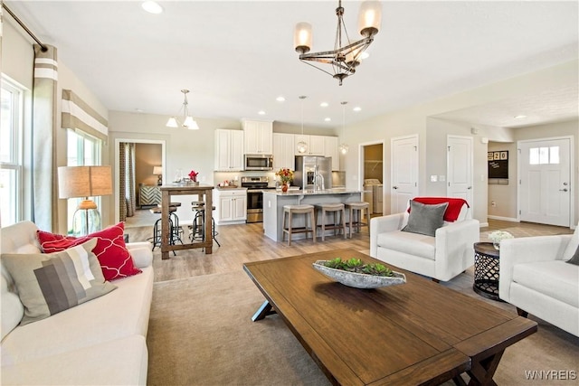 living area with recessed lighting, baseboards, light wood-type flooring, and an inviting chandelier