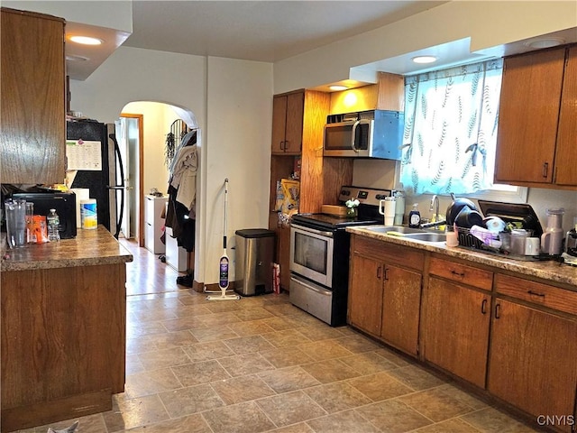 220 Odell Ave, Union, NY 13760 - kitchen featuring arched walkways, a sink, stainless steel appliances, stone finish floor, and brown cabinets