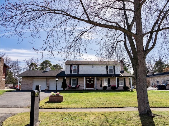 traditional home with aphalt driveway, brick siding, a garage, and a front yard
