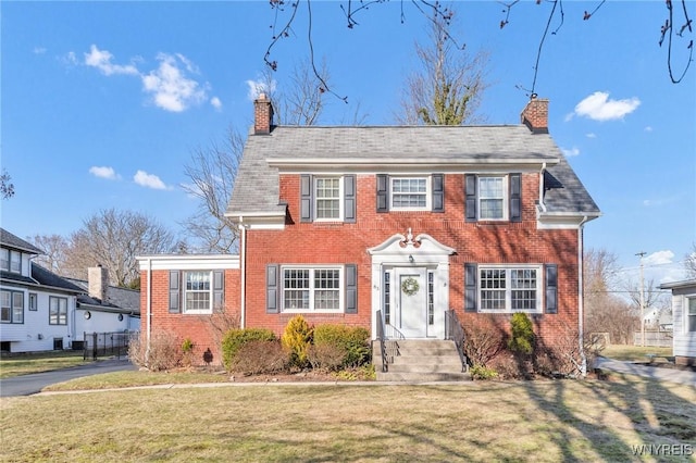 colonial home with brick siding, a front lawn, and a chimney