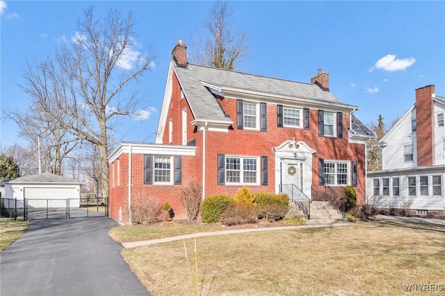 colonial house featuring brick siding, a chimney, a front lawn, and a gate