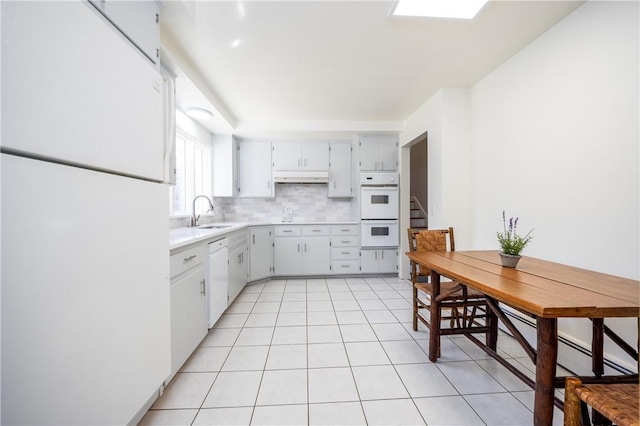 kitchen featuring under cabinet range hood, light countertops, decorative backsplash, white appliances, and a sink