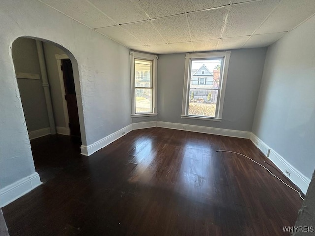 spare room featuring a drop ceiling, baseboards, arched walkways, and wood finished floors