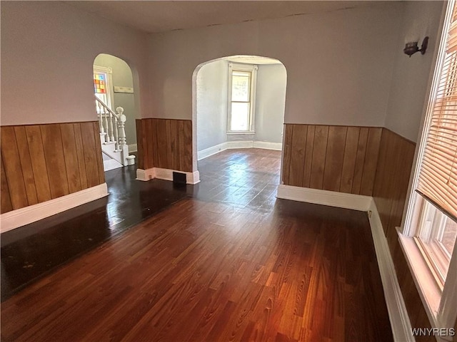empty room with a wainscoted wall, wood finished floors, arched walkways, and wood walls