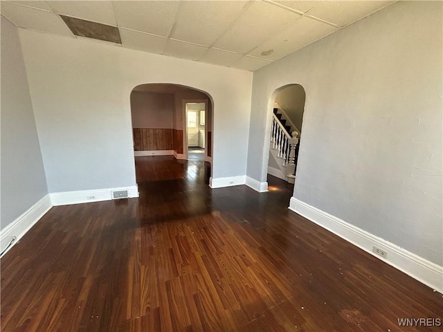 spare room with arched walkways, stairs, a paneled ceiling, and wood finished floors