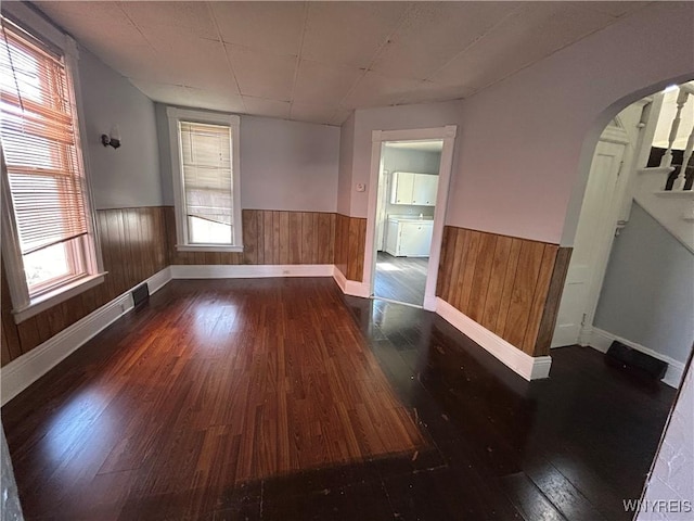 unfurnished room featuring arched walkways, a wainscoted wall, wooden walls, and wood-type flooring