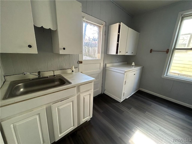 clothes washing area featuring baseboards, a healthy amount of sunlight, dark wood-style flooring, and a sink