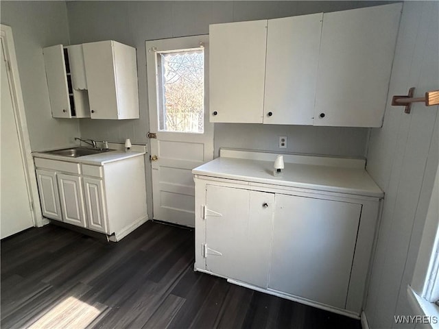 kitchen with light countertops, white cabinets, dark wood-type flooring, and a sink